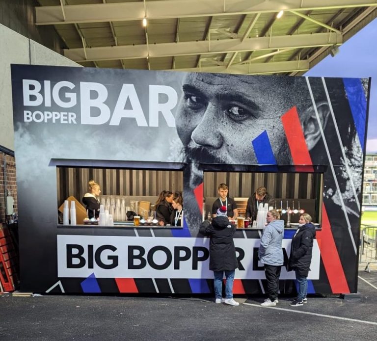 A bar stall featuring the name "Big Bopper Bar" with customers being served drinks.